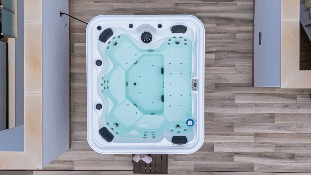 Top-down view of a modern square hot tub filled with water, jets visible, set on a wood-look floor